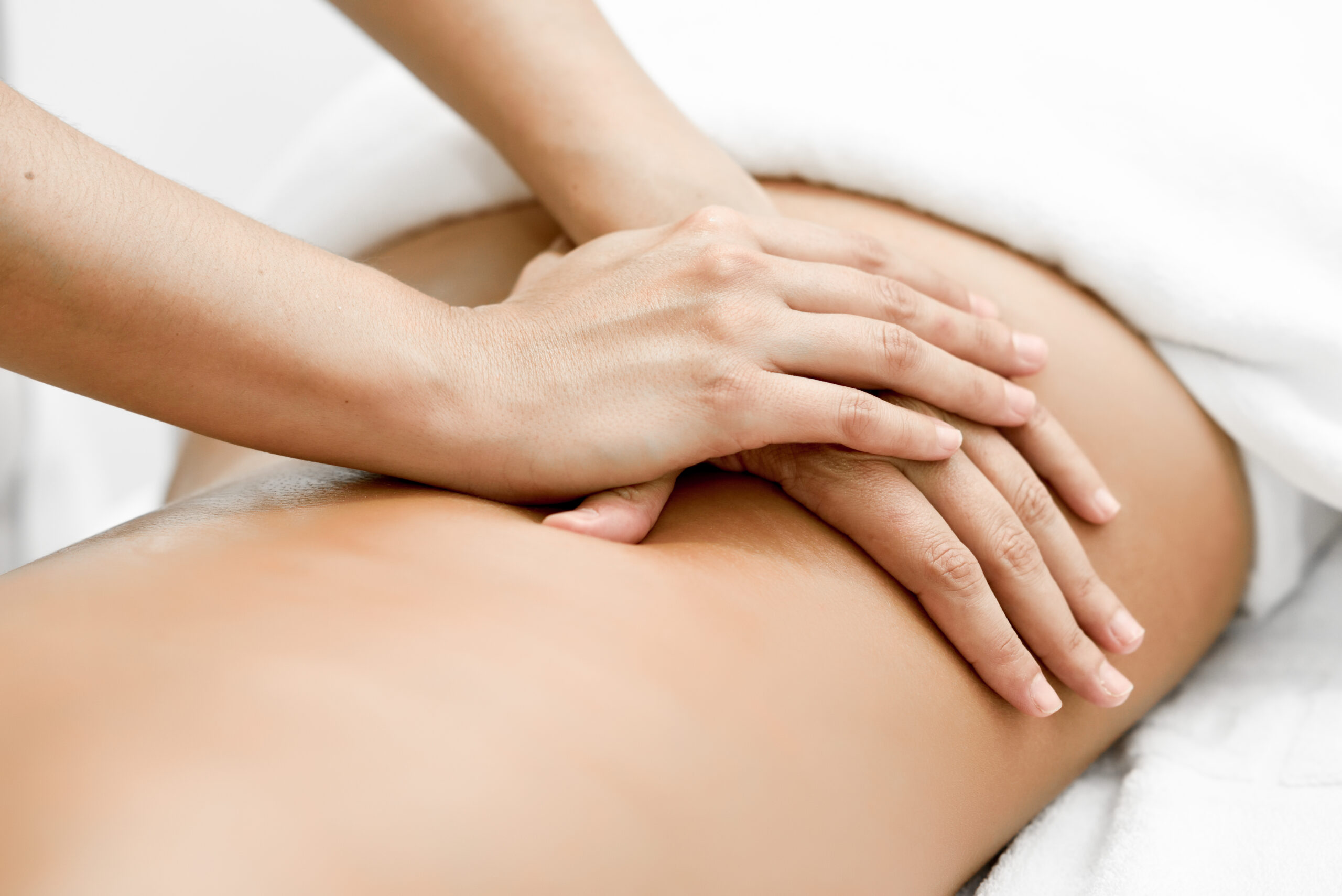 Young,Woman,Receiving,A,Back,Massage,In,A,Spa,Center. Hands performing deep tissue massage on client’s lower back